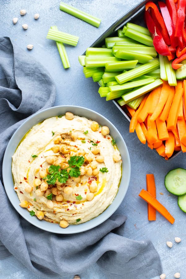 The best hummus recipe in a grey serving bowl next to a tray of vegetables to serve with it.