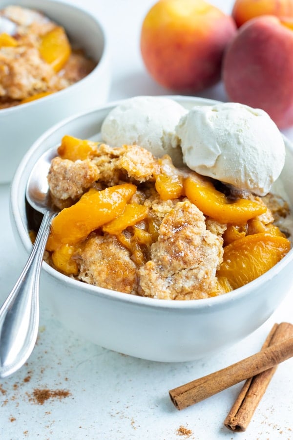 A big bowl of healthy, homemade cobbler made with tender peaches is topped with two scoops of vanilla ice-cream.
