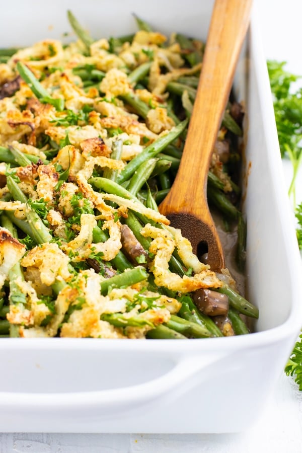 Green bean casserole recipe in a white baking dish with a wooden spoon.