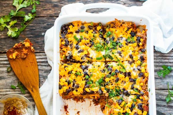 A white casserole dish full of a ground turkey taco lasagna recipe with a wooden spoon next to it.
