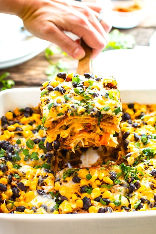 A hand scooping out a big piece of a ground turkey taco lasagna casserole.
