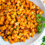Oven roasted sweet potato recipe in a gray bowl surrounded by herbs.
