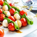 Caprese salad on wooden skewers with balsamic glaze in the background.