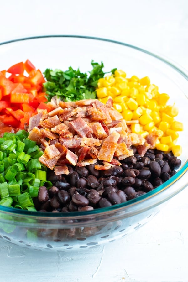 Ingredients for a black bean and corn salsa recipe in a clear Pyrex bowl.