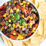 Black bean bacon dip for a party appetizer in a white bowl surrounded by corn tortilla chips.