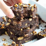 A hand grabbing a fudgy black bean brownie from a stack of brownies.