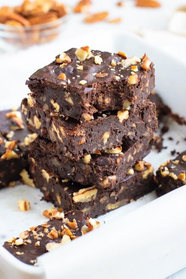 A stack of black bean brownies with pecans in a white baking dish.