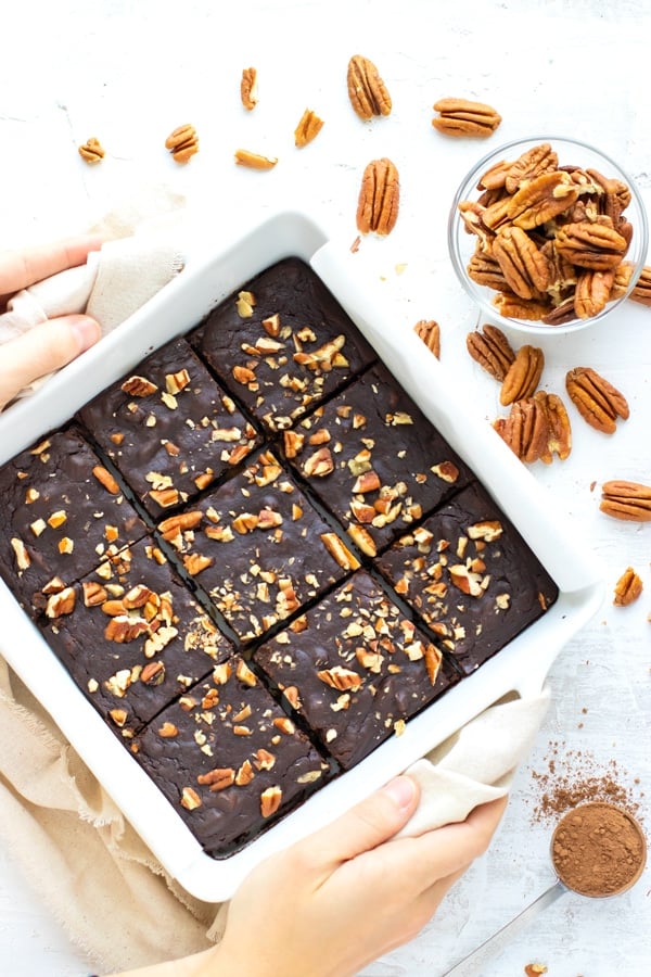 A white baking dish full of black bean brownies next to a bowl full of pecans.