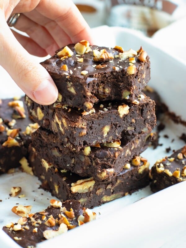 A hand grabbing a fudgy black bean brownie from a stack of brownies.