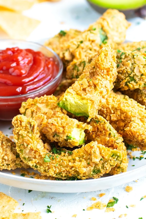 A stack of avocado fries next to a bowl of ketchup.