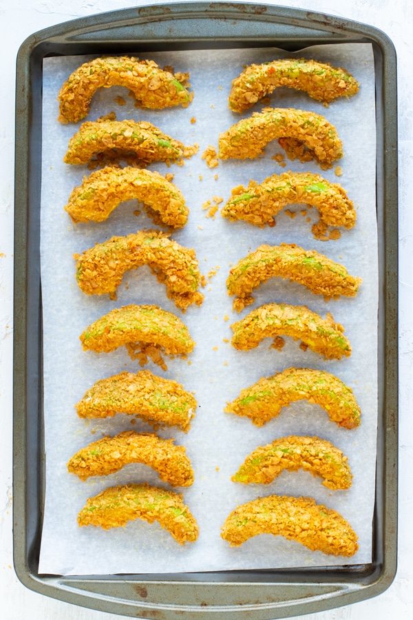 Tortilla chip crusted avocado fries recipe on a parchment paper-lined baking sheet.