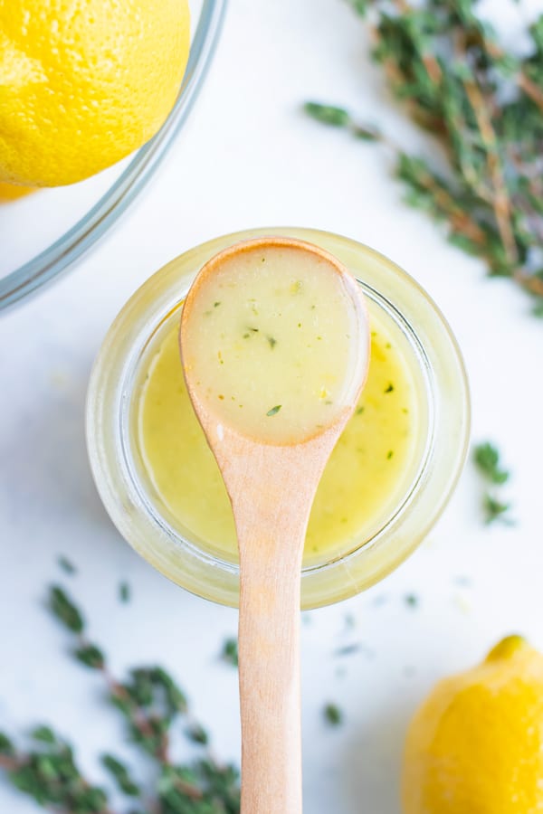 Lemon vinaigrette is kept in a jar on the counter with fresh herbs and lemons.