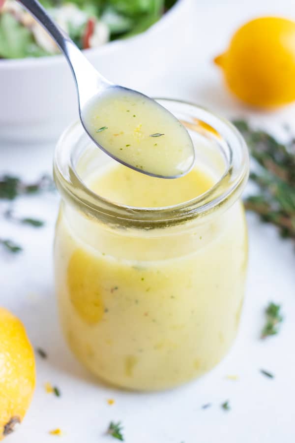A spoon is used to lift the lemon vinaigrette from the jar.