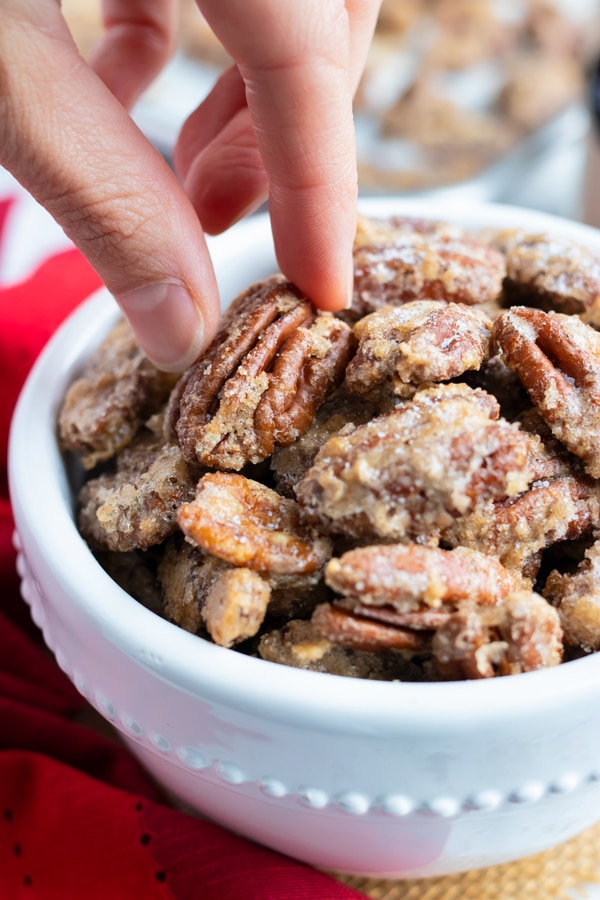 A hand picking up a spiced candied pecan from a snack bowl.