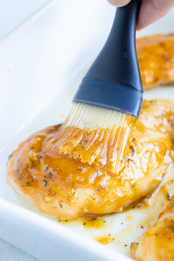 A pastry brush that is basting a piece of chicken immediately after being removed from the oven.