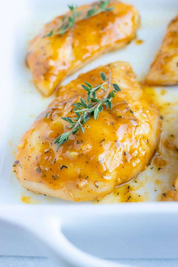A white casserole dish with chicken breasts that have been baked in the oven and are covered in a honey-colored sauce.