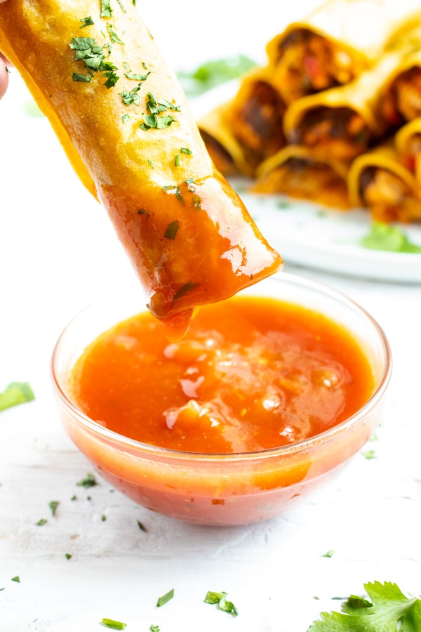 A baked chicken taquito being dipped into a glass bowl of salsa.