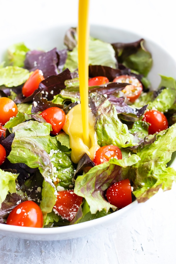 Honey mustard dressing being poured onto a salad with mixed greens and tomatoes.