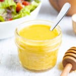 A small glass container that is full of mustard vinaigrette with a silver spoon.