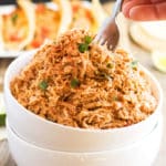A hand dipping a silver fork inside a white bowl filled with easy shredded chicken made with salsa.