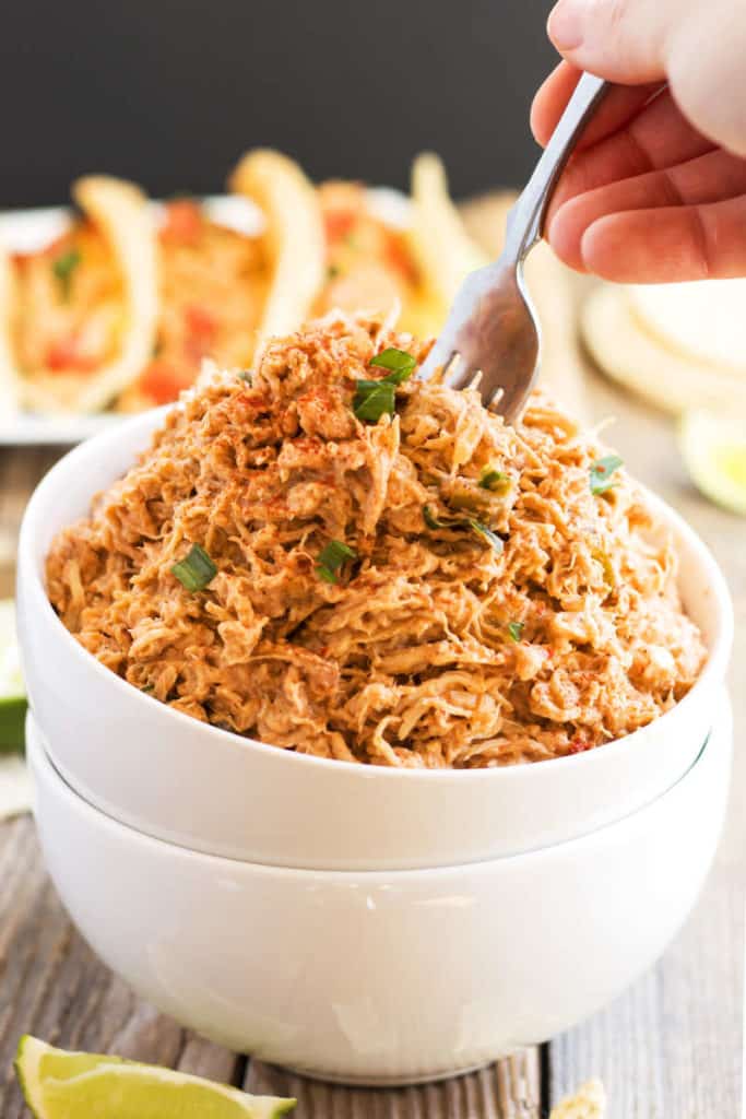 A hand dipping a silver fork inside a white bowl filled with easy shredded chicken made with salsa.