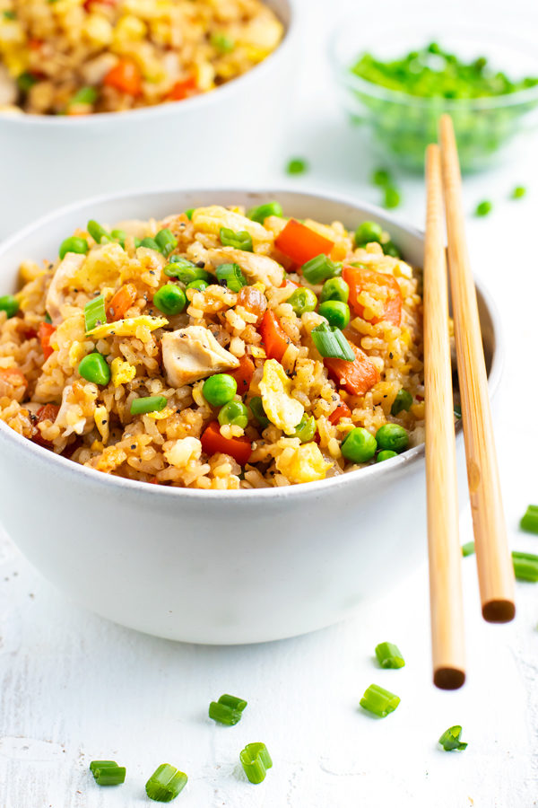 A white bowl full of chicken fried rice recipe with a pair of chopsticks.