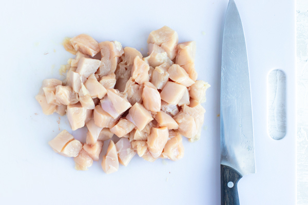 Cubed chicken on a white cutting board next to a knife.