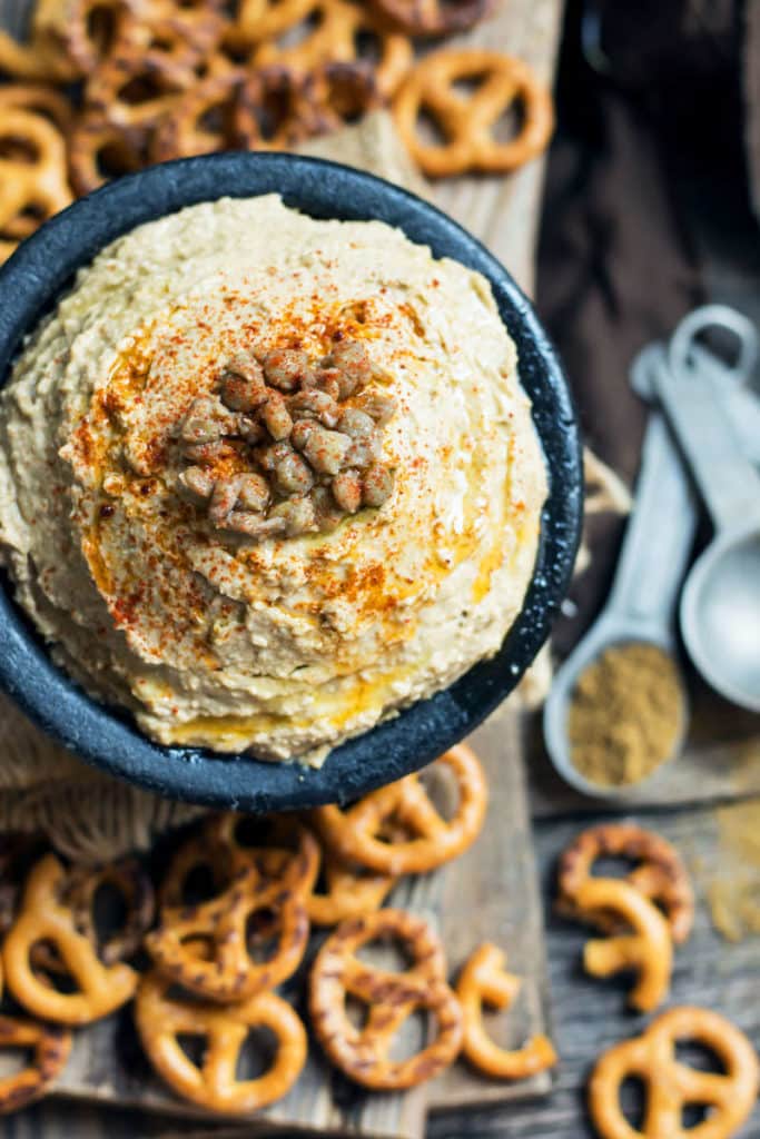 A lentil hummus recipe in a black bowl surrounded by pretzels for an easy snack.
