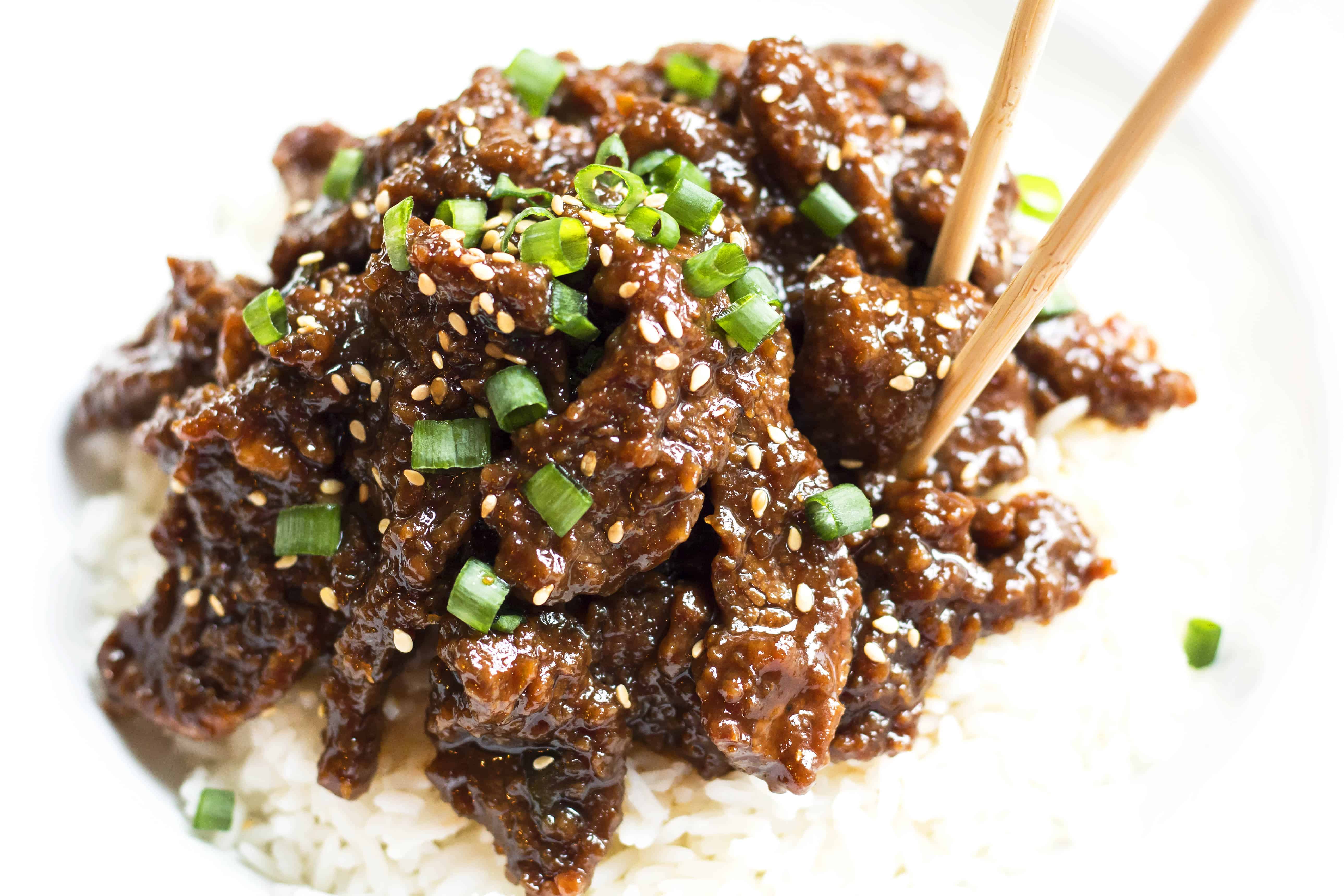 A close up picture of chopsticks picking up a piece of Copycat Mongolian Beef for dinner.
