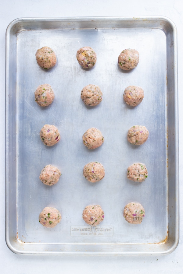 The turkey meatballs are spaced apart on a large baking sheet before being cooked in the oven.