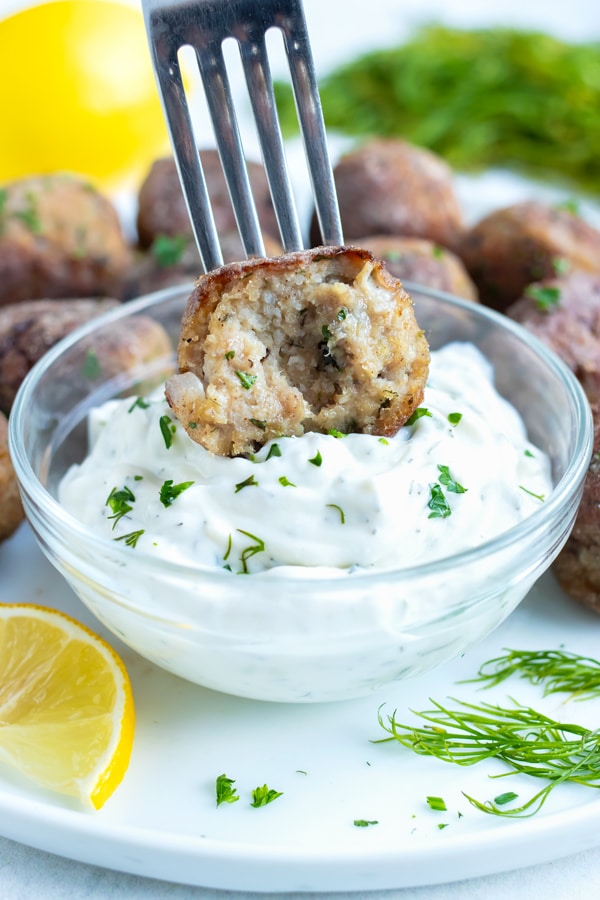 A pan seared, oven-baked turkey meatball is dipped into a creamy tzatziki sauce.