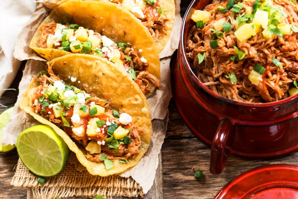 Tacos made with a pork tacos recipe on a table with pulled pork on the side.