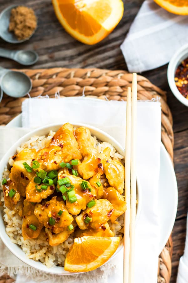 An overhead picture of gluten-free orange chicken in a bowl with orange slices and chopsticks for dinner.