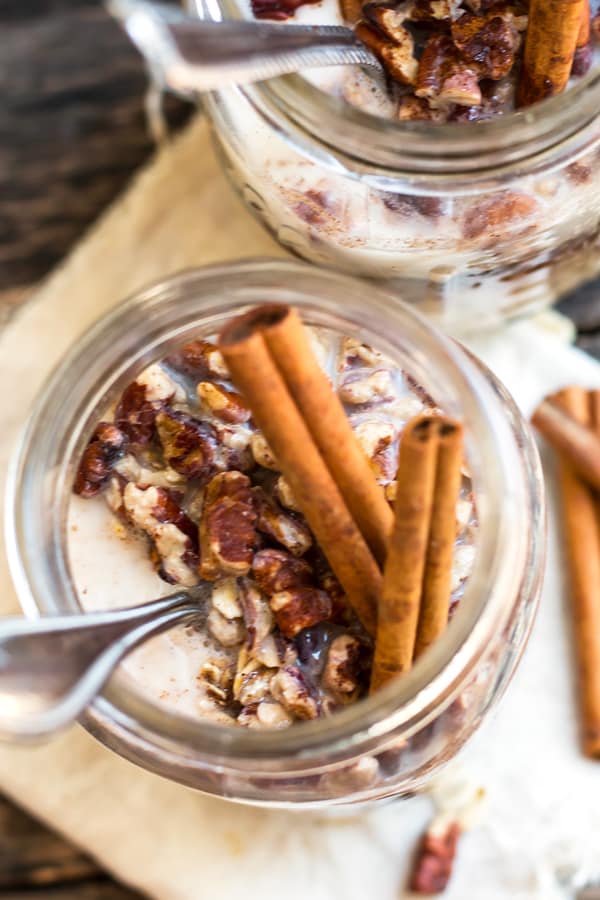 An overhead picture of a gluten-free overnight oats recipe in a jar with cinnamon sticks as a garnish.