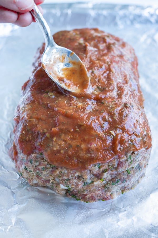 A spoon is used to spread the special glaze onto the meatloaf.