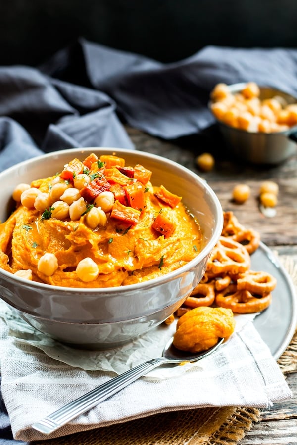 A serving bowl filled with Roasted Sweet Potato Hummus with pretzels on the side.