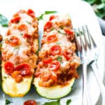 Two sausage zucchini boats on a white plate with two forks on the side.