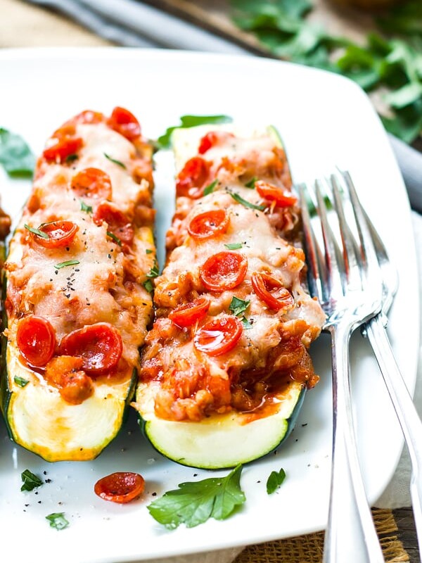 Two sausage zucchini boats on a white plate with two forks on the side.