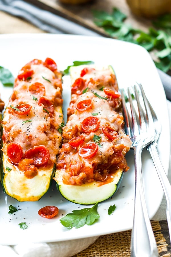 Two sausage zucchini boats on a white plate with two forks on the side.