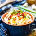 Mashed cauliflower potatoes topped with green onions and bacon on a table for a healthy dinner.