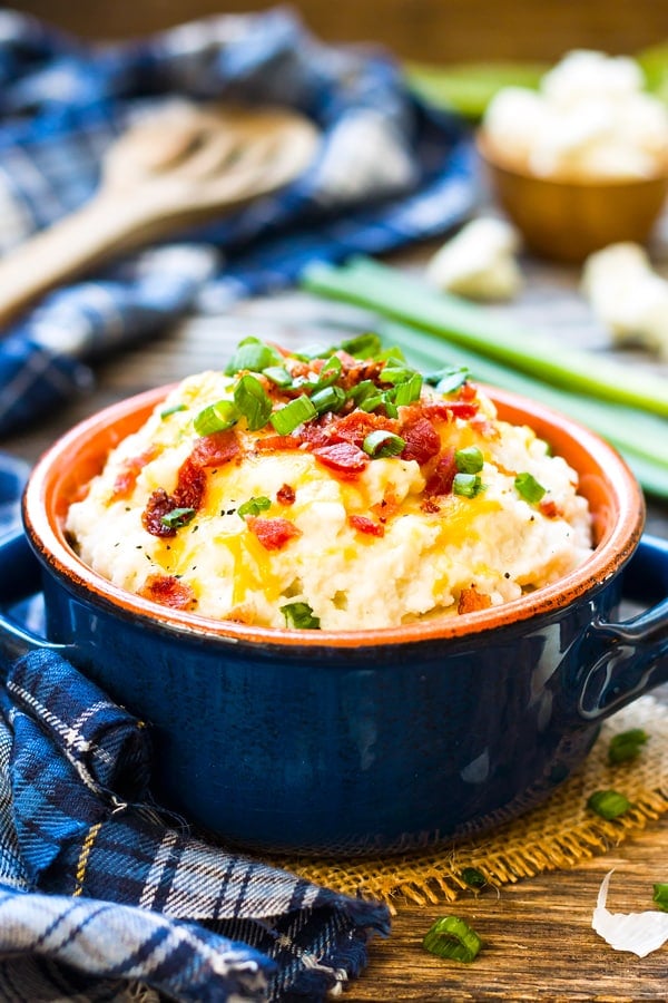 Mashed cauliflower potatoes topped with green onions and bacon on a table for a healthy dinner.