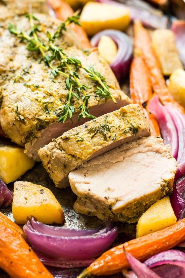 A pork tenderloin recipe surrounded by apples and vegetables for a healthy dinner.