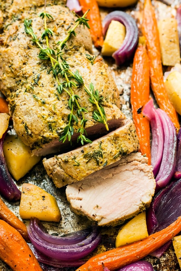 A mustard pork tenderloin sliced into two pieces and surrounded by vegetables.