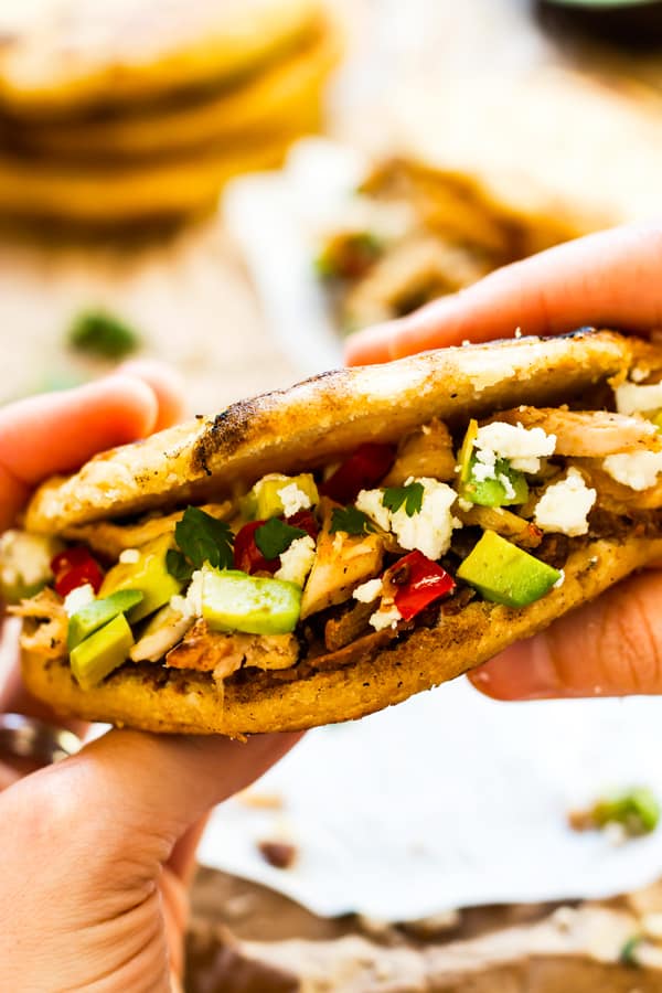 A pair of hands holding a stuffed arepas with chicken and avocados for a healthy lunch.