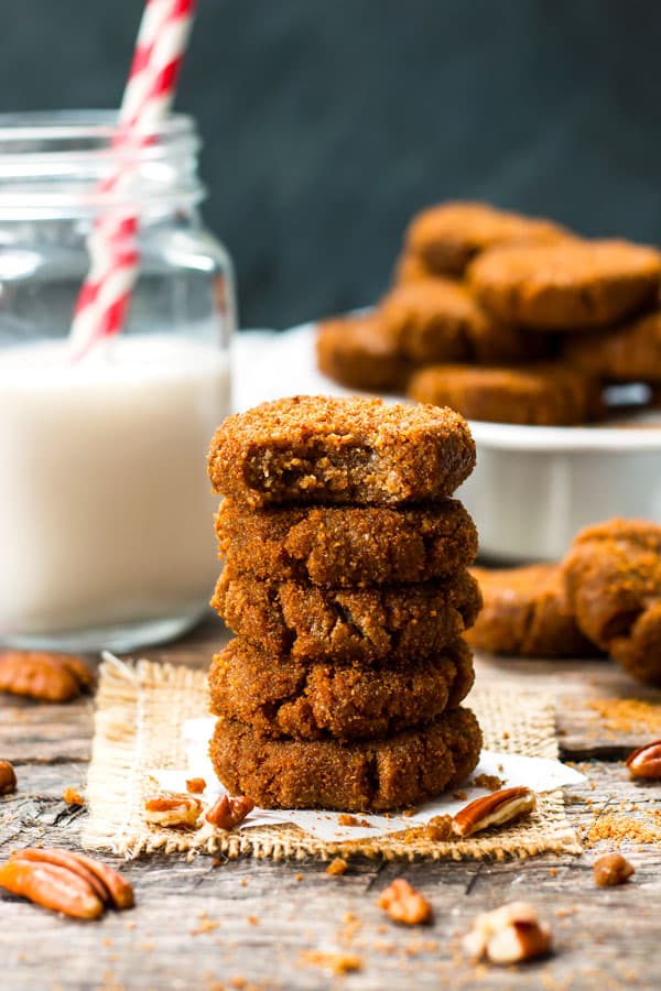 A pile of paleo molasses cookies on parchment paper with a glass of milk and two straws.