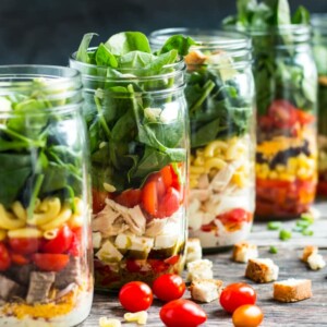 A line of mason jar lunches using fresh vegetables and other ingredients.