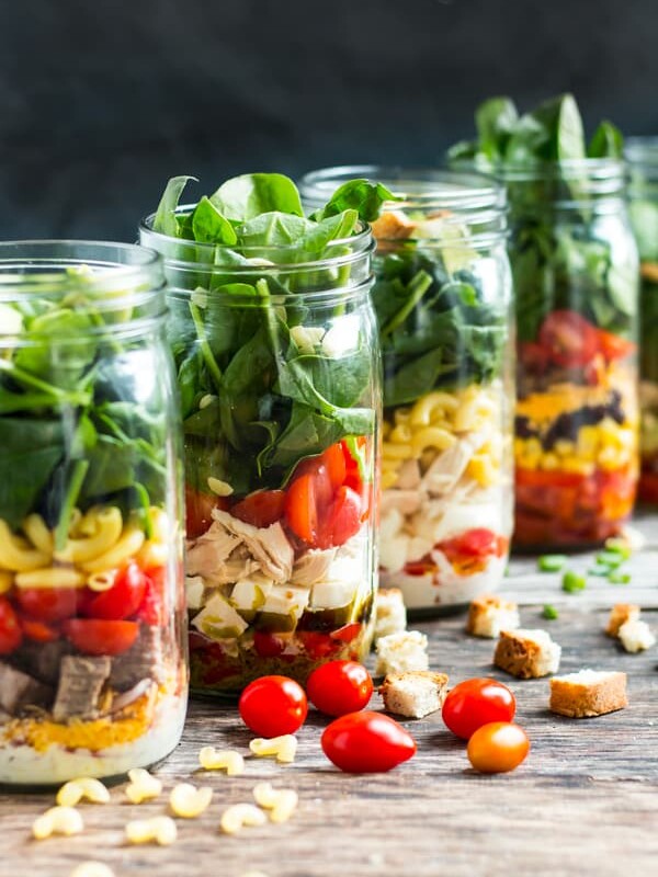 A line of mason jar lunches using fresh vegetables and other ingredients.