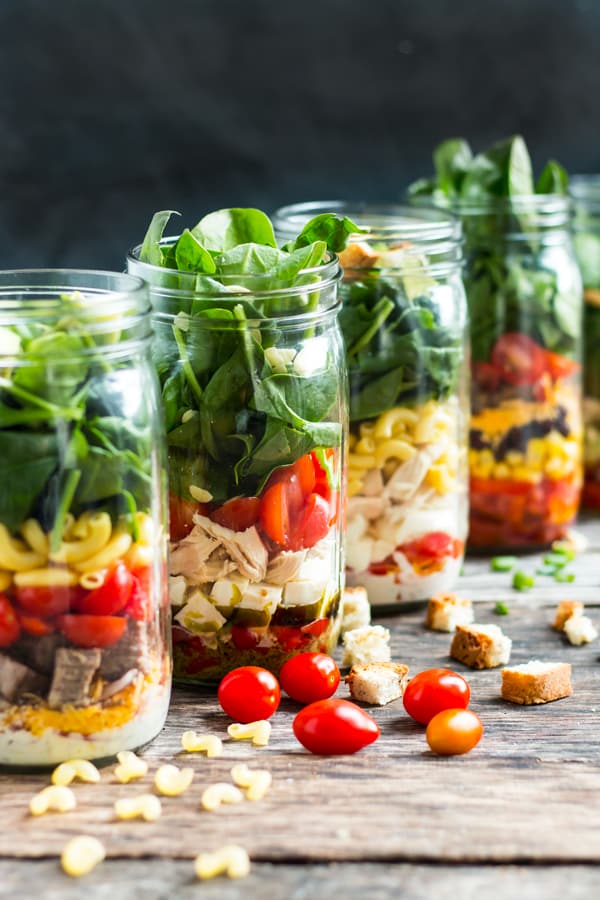 A line of mason jar lunches using fresh vegetables and other ingredients.