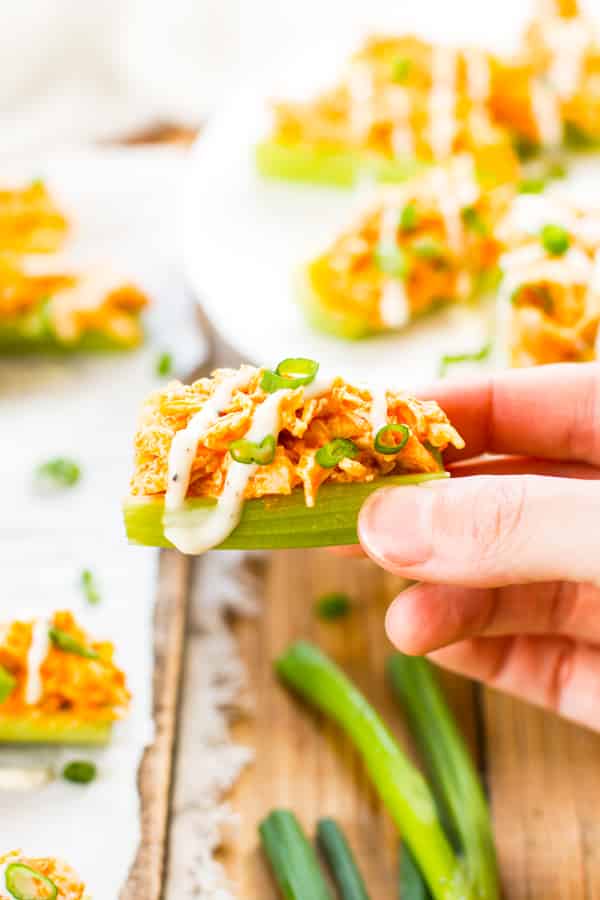 A hand holding a celery stick with a buffalo chicken recipe for a quick appetizer.
