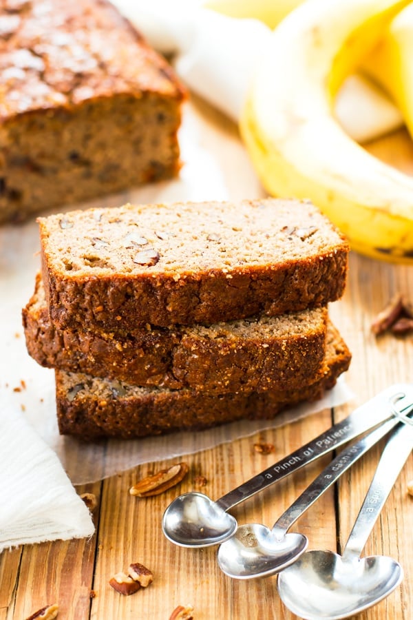 Three slices of gluten-free banana bread with sliver measuring spoons on a table.